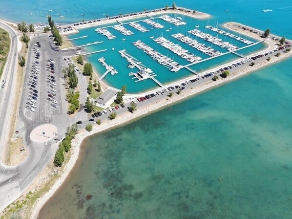 Vue aérienne d’une marina où sont amarrés de nombreux bateaux, avec un espace de stationnement et une route menant à la marina.