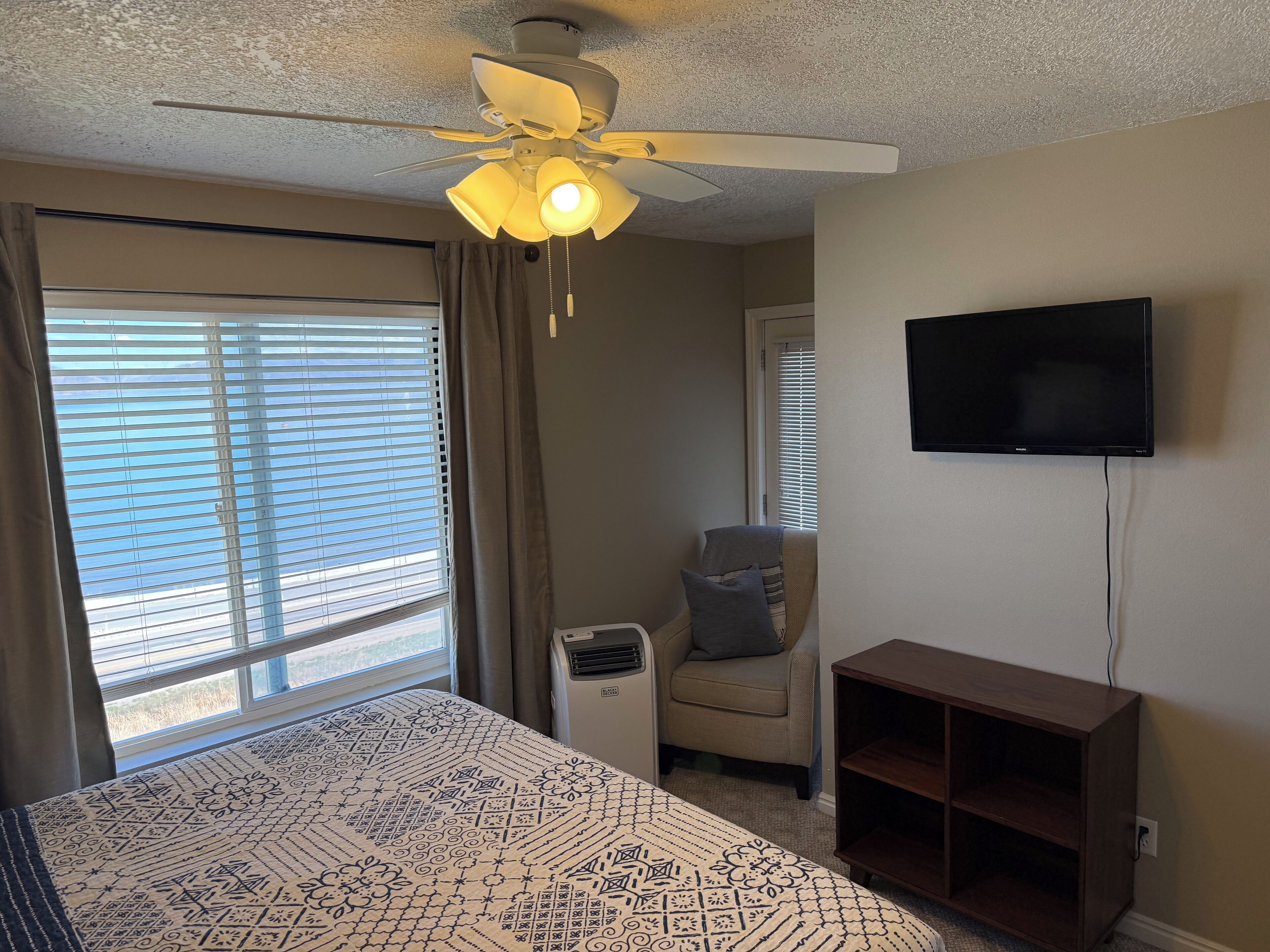 Quarto com cama, ventilador de teto, televisão e janela com persianas.