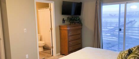 Un dormitorio con cama, cómoda, televisor y vista a un paisaje nevado a través de un ventanal grande.