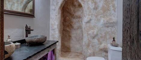 A rustic bathroom with a stone wall, wooden ceiling, and a wooden vanity with a bowl sink.