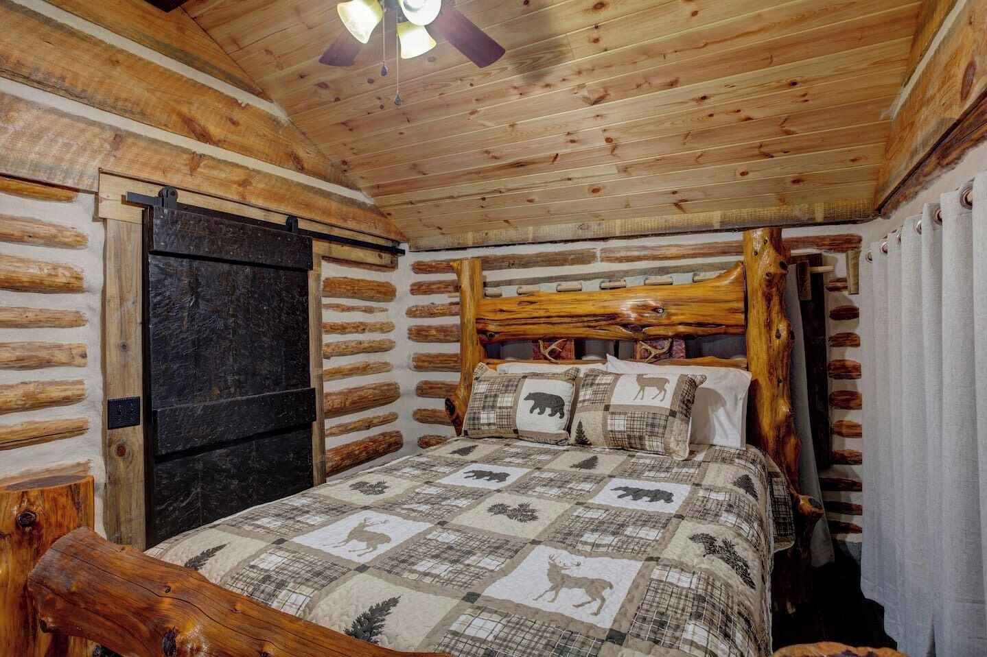 Ein Schlafzimmer in einer Blockhütte mit Bett, Holz-Kopfteil und Deckenventilator.