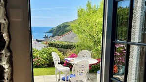 A patio with white chairs and a table, a stone wall, and a view of the sea and hills. - Little Gwyn. 3 min walk to Beach! Gorgeous views out to sea. (Gorran Haven)