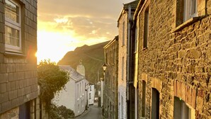 A narrow street lined with stone buildings, a clear sky, and a distant mountain. - Little Gwyn. 3 min walk to Beach! Gorgeous views out to sea. (Gorran Haven)