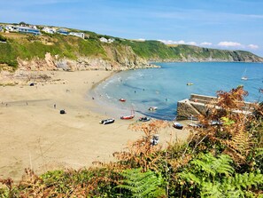 Une plage côtière offrant une vue dégagée sur la mer, une falaise rocheuse et quelques bateaux.