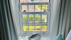 A bedroom with a view of the ocean through a window with curtains. - Little Gwyn. 3 min walk to Beach! Gorgeous views out to sea. (Gorran Haven)