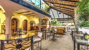 Un espace de restauration intérieur doté de plusieurs tables et chaises, d’une cloison en verre et d’un mur végétal tropical.