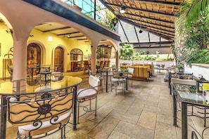 An indoor dining area with multiple tables and chairs, a glass partition, and a tropical plant wall.