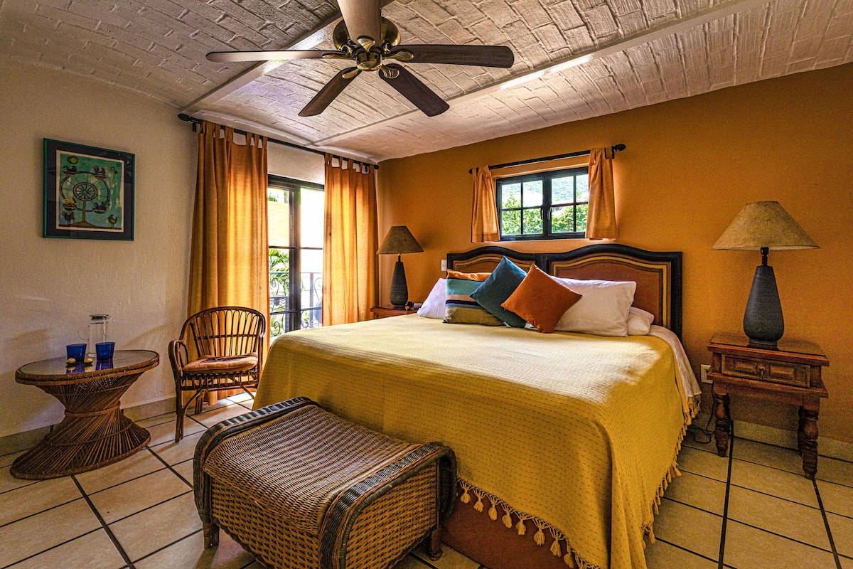 A hotel room with a bed, a chair, a small table, and a ceiling fan.