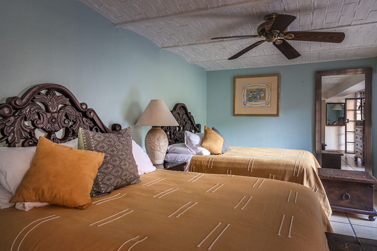 A room with two beds, a ceiling fan, a lamp, and a framed picture on the wall.