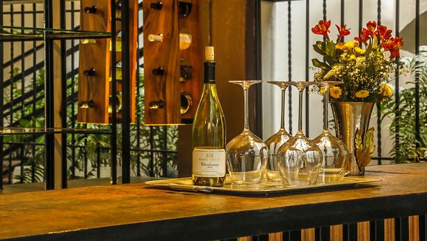 Une bouteille de vin, plusieurs verres à vin et un vase rempli de fleurs, le tout posé sur le comptoir en bois d’un bar.