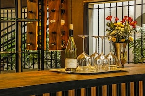 Une bouteille de vin, plusieurs verres à vin et un vase rempli de fleurs, le tout posé sur le comptoir en bois d’un bar.