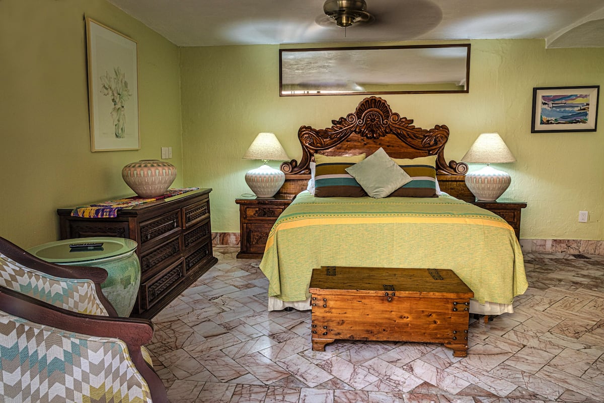 A bedroom with a bed, two nightstands, a dresser, a chair, a wooden chest, and a ceiling fan.