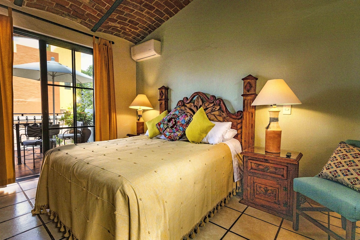 A hotel room with a large bed, two bedside tables with lamps, a wooden headboard, and a view of the outside patio.