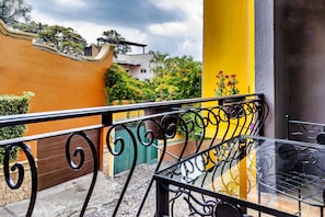 A balcony with a metal railing, a yellow wall, and a green door.