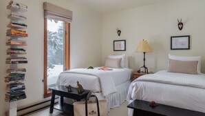 A hotel room with two beds, a bookshelf, a desk, a lamp, and a window with a view of trees. - Outpost: Huckleberry 3124 -Wood burning fireplace! (Wilson)