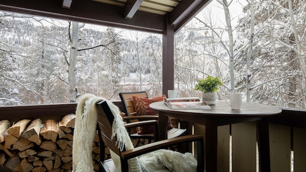 A covered outdoor seating area with a table, chairs, and a view of a snowy forest. - Outpost: Huckleberry 3124 -Wood burning fireplace! (Wilson)