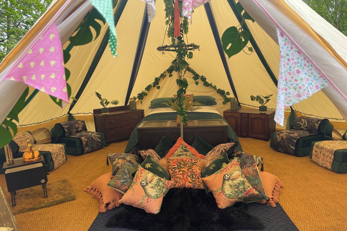 Een tent met een bed, kussens, een nachtkastje en een klein tafeltje.