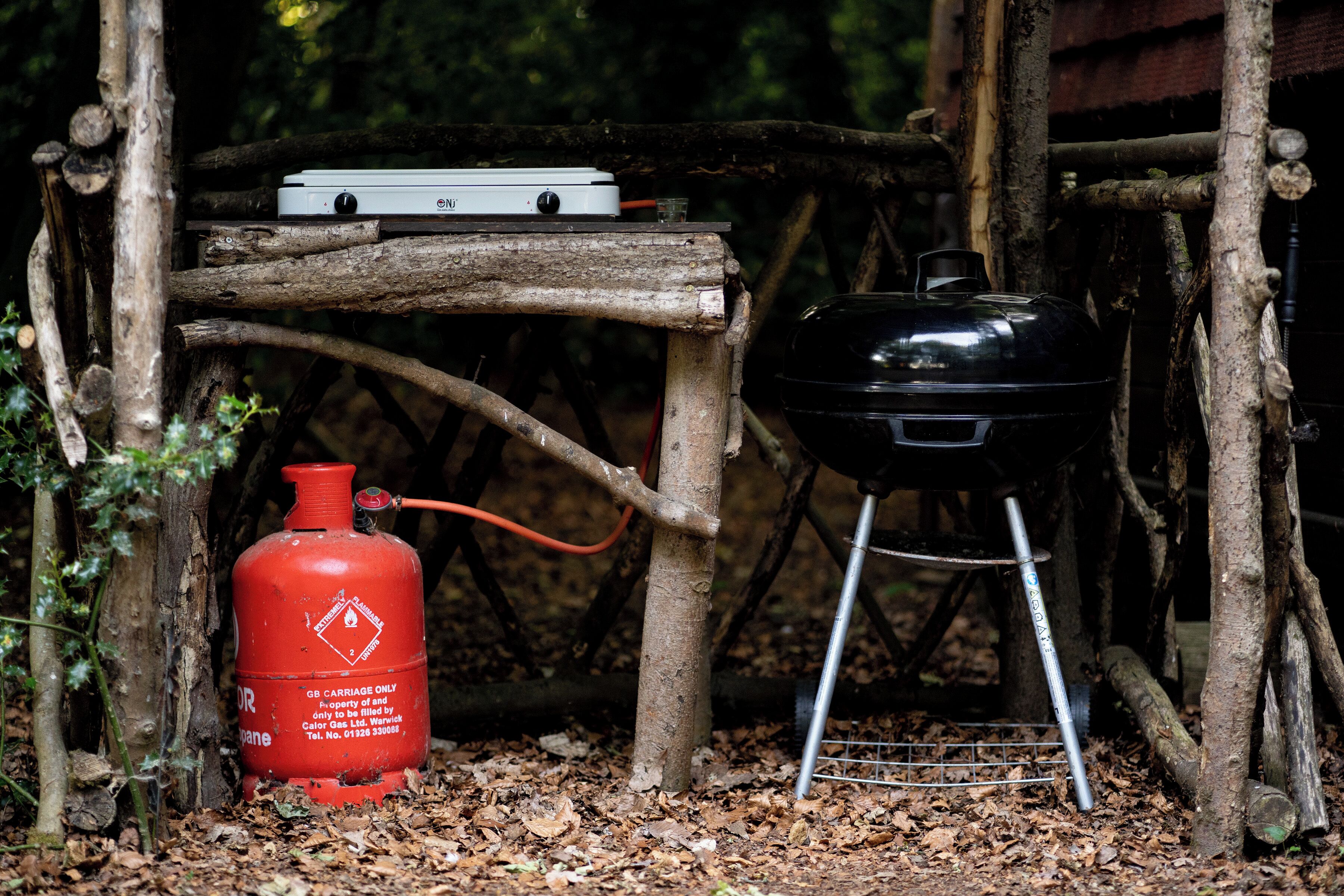 A portable grill and a gas cylinder in a wooded area.