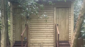 Un abri en bois avec deux escaliers menant à une porte, entouré d’arbres et recouvert de feuilles.