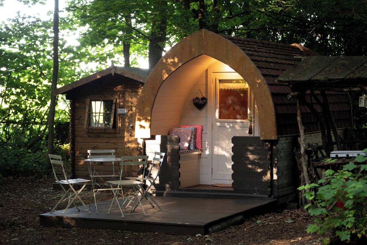 Een houten blokhut met een veranda, een eettafel met stoelen en een hartvormige decoratie aan de wand.