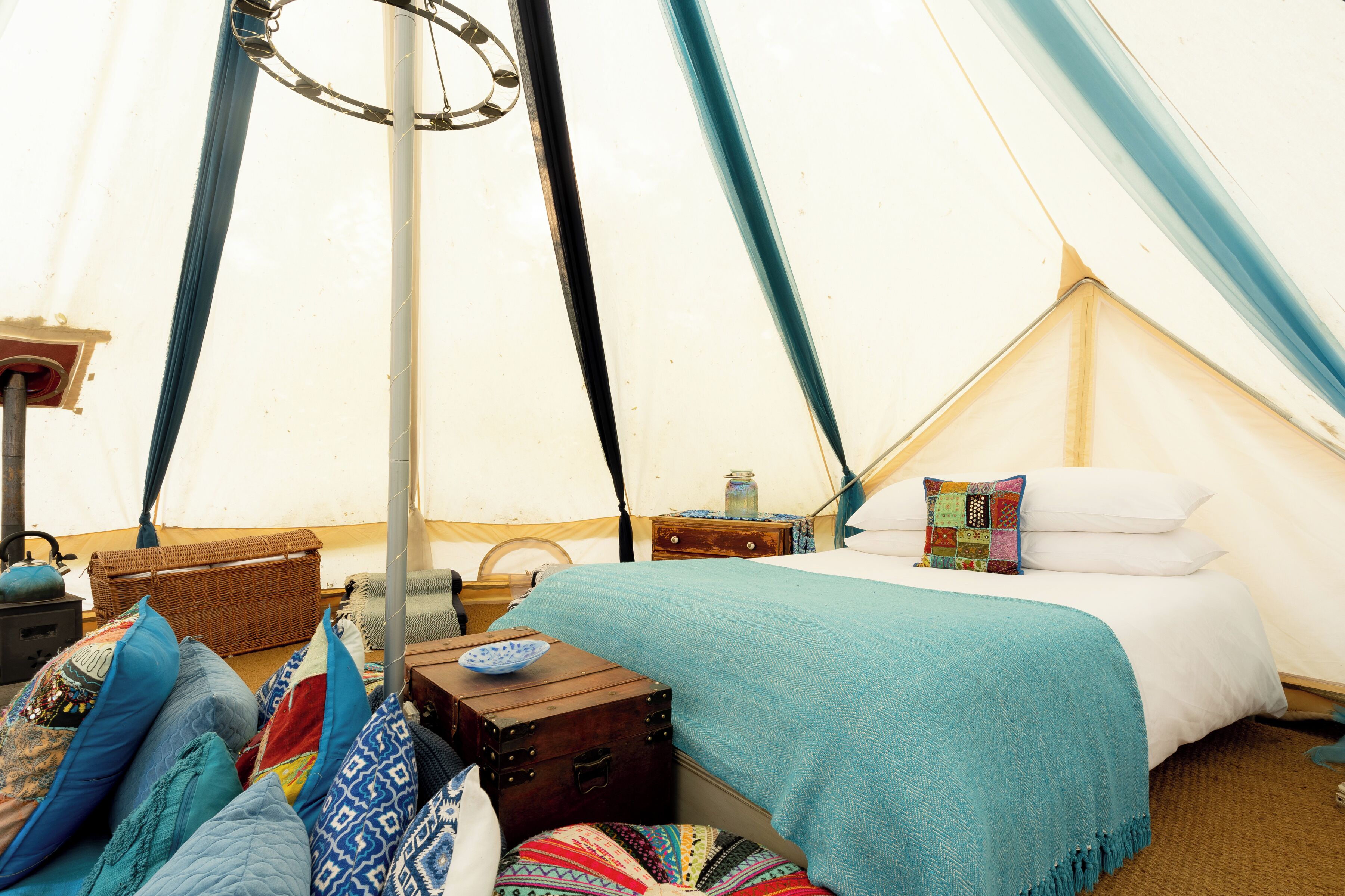 A tented accommodation with a bed, pillows, a chest of drawers, and a small table.