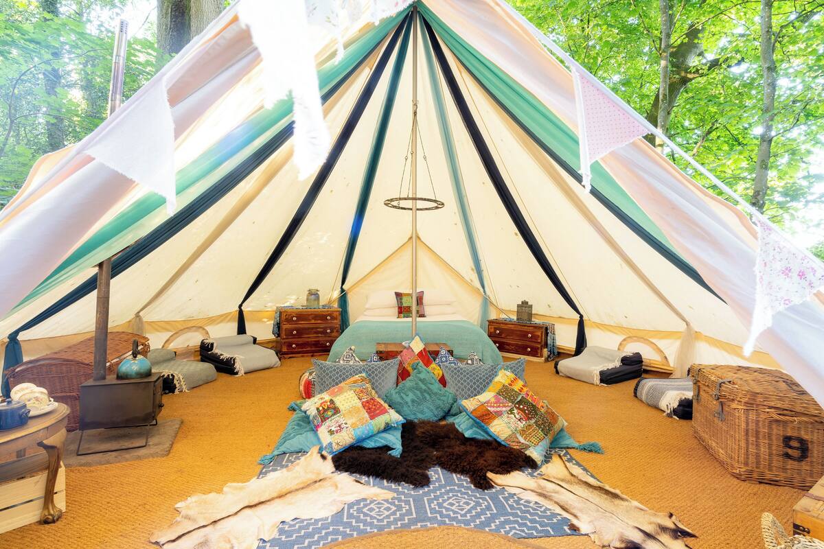 Een tent met een bed, kussens, een deken, een tafeltje en een kist.