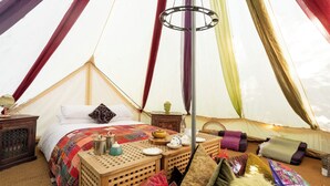 L’intérieur accueillant d’une tente, avec un lit, une petite table et une bouilloire, ainsi que diverses couvertures et coussins.