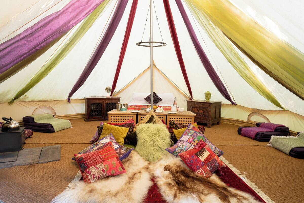 Een gezellig interieur van een tent met een centrale tafel, kleurrijke kussens en een vachttapijt.