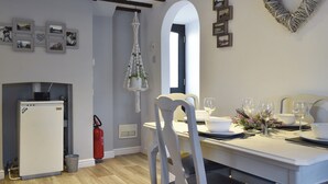 En matplats med ett vitt bord dukat för fyra personer, ett vitt kylskåp, en brandsläckare och en hängande lampa i makramé.