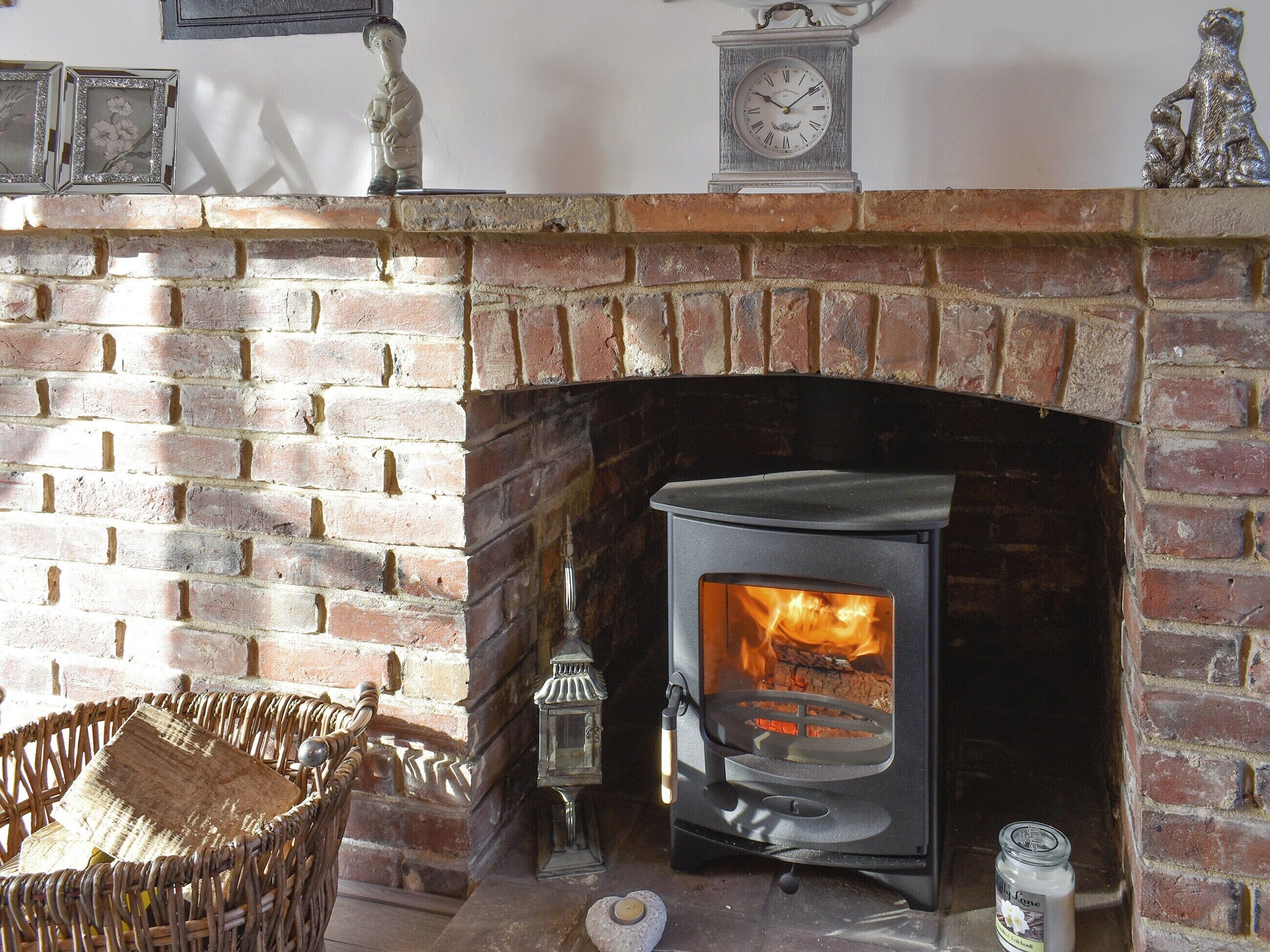 A brick fireplace with a modern wood-burning stove, a clock, and decorative items on the mantel.