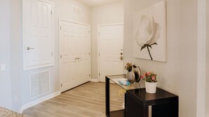 A hallway with white doors, a vent, a framed artwork of a flower, and a small table with a vase and flowers. - Serene Waters at Vista Cay Resort (Orlando)