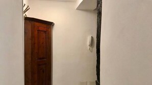 A narrow hallway with a wooden door on the left and a white wall with a white switchboard on the right. - Navel of Parma (Parma)