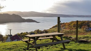 Una mesa de picnic sobre una colina cubierta de césped con vistas a un lago y montañas a lo lejos.