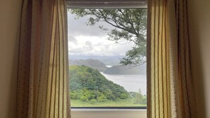 Una ventana con cortinas, vista a un lago y un paisaje montañoso.