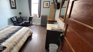 A hotel room with a bed, a desk, a chair, a window with curtains, a radiator, a sink, and a mirror. - Dillon Tap House Beaverhead Room (Dillon)