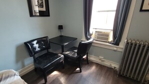 A small room with a bed, a desk, two chairs, a radiator, and a window with curtains. - Dillon Tap House Beaverhead Room (Dillon)