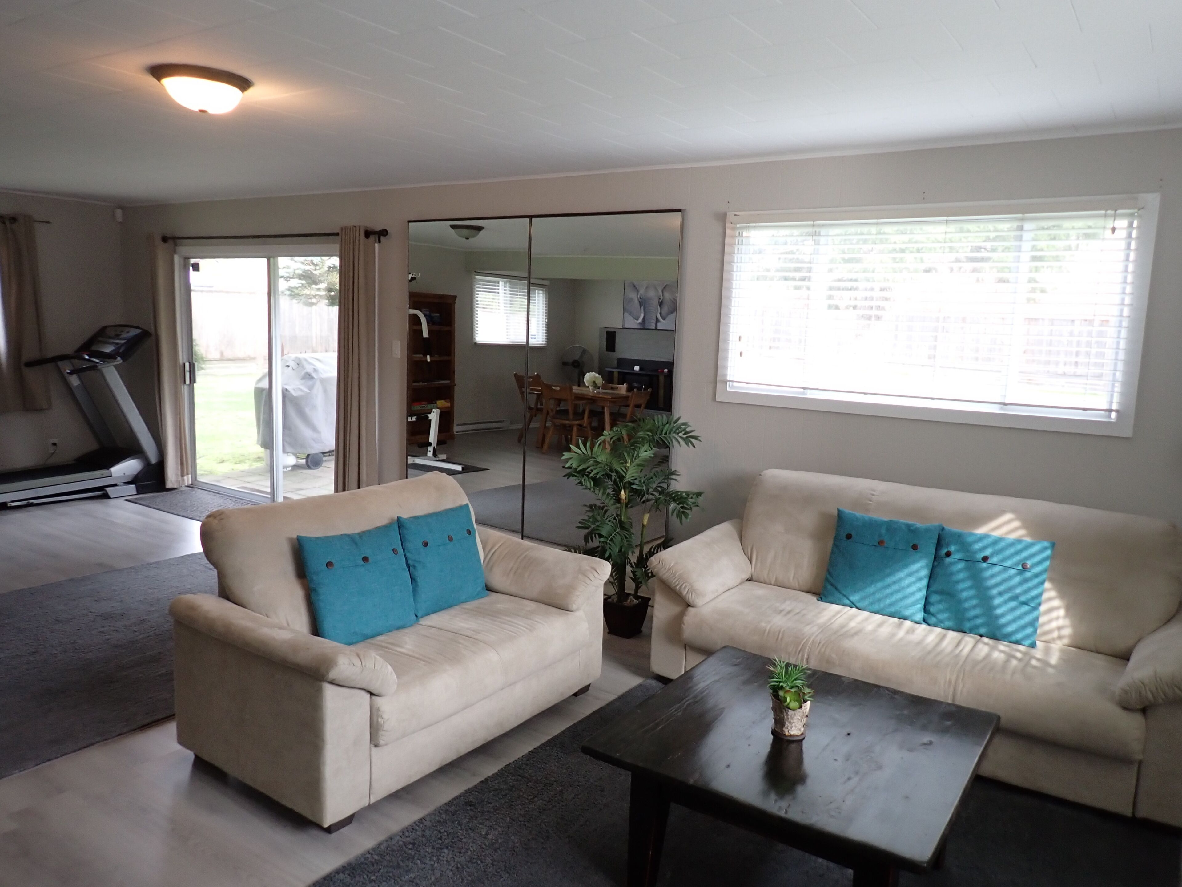 A living room with a treadmill, two sofas, a coffee table, and a large window.