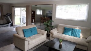 A living room with a treadmill, two sofas, a coffee table, and a large window. - Spacious 2 bedroom suite on private lot (Pemberton)