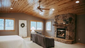 A room with a fireplace, a bed, a covered couch, and a ceiling fan. - Experience Starbuck charm in our spacious 5-bedroom retreat (Starbuck)