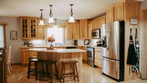 A kitchen with wooden cabinets, a stainless steel refrigerator, a built-in oven, and a large island with stools. - Experience Starbuck charm in our spacious 5-bedroom retreat (Starbuck)