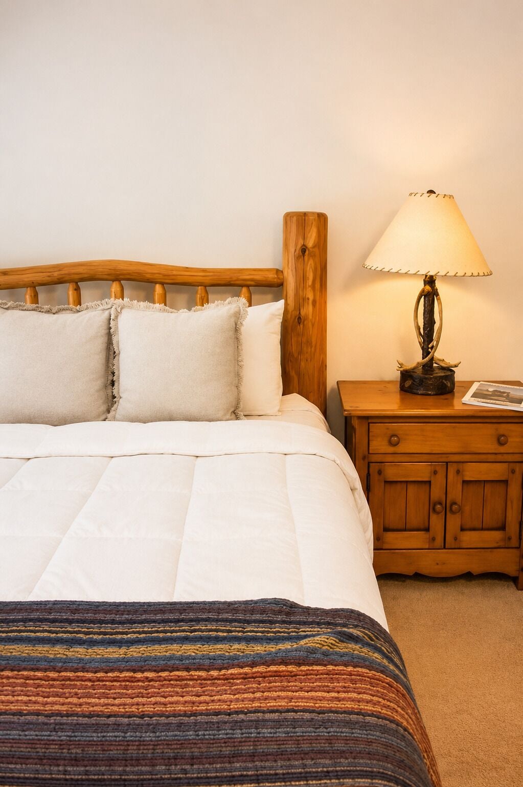 A bed with a wooden headboard, a bedside table with a lamp, and a patterned throw blanket.