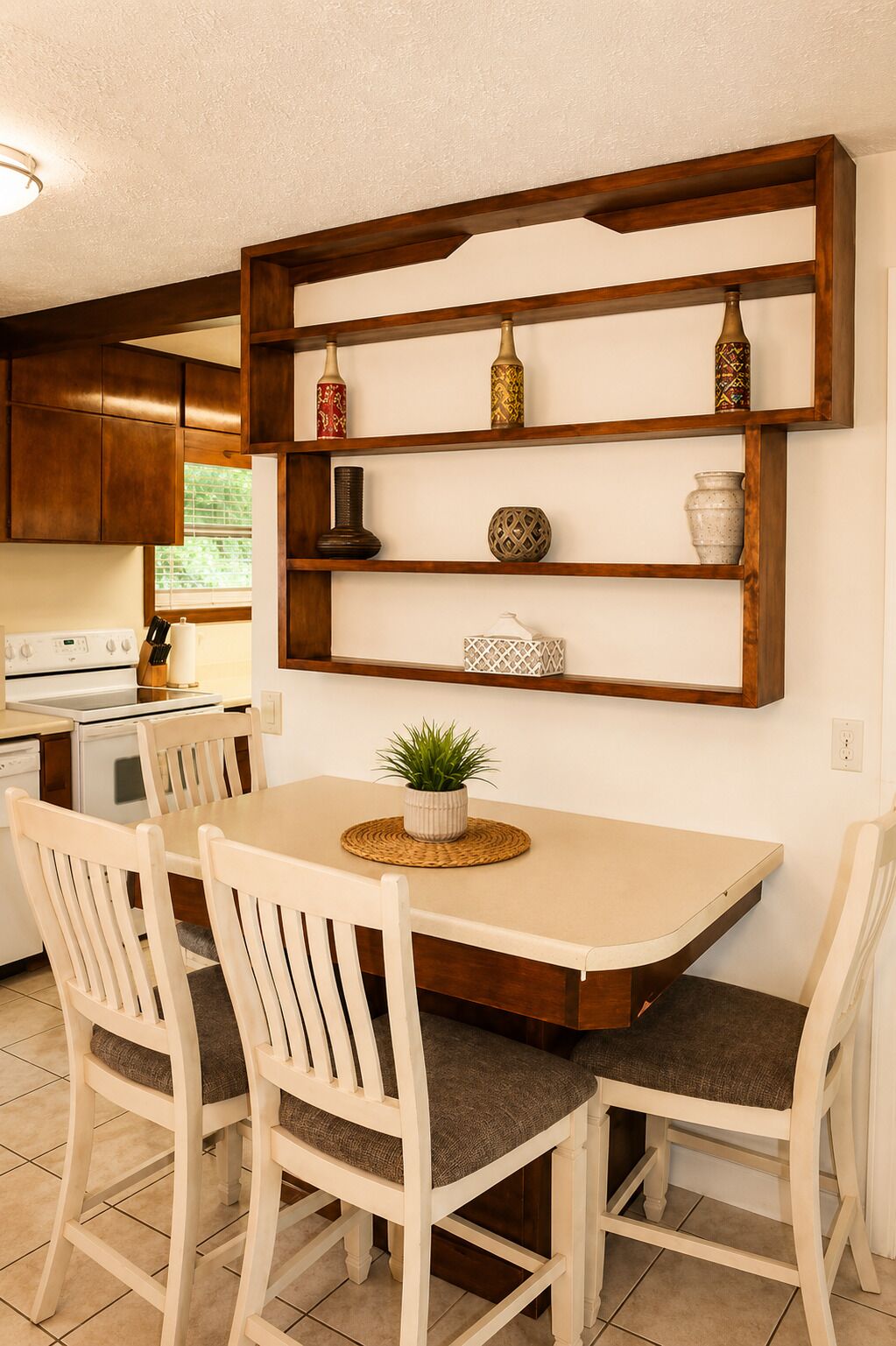 A kitchen with a wooden shelf, a dining table with four chairs, and a potted plant on the table.