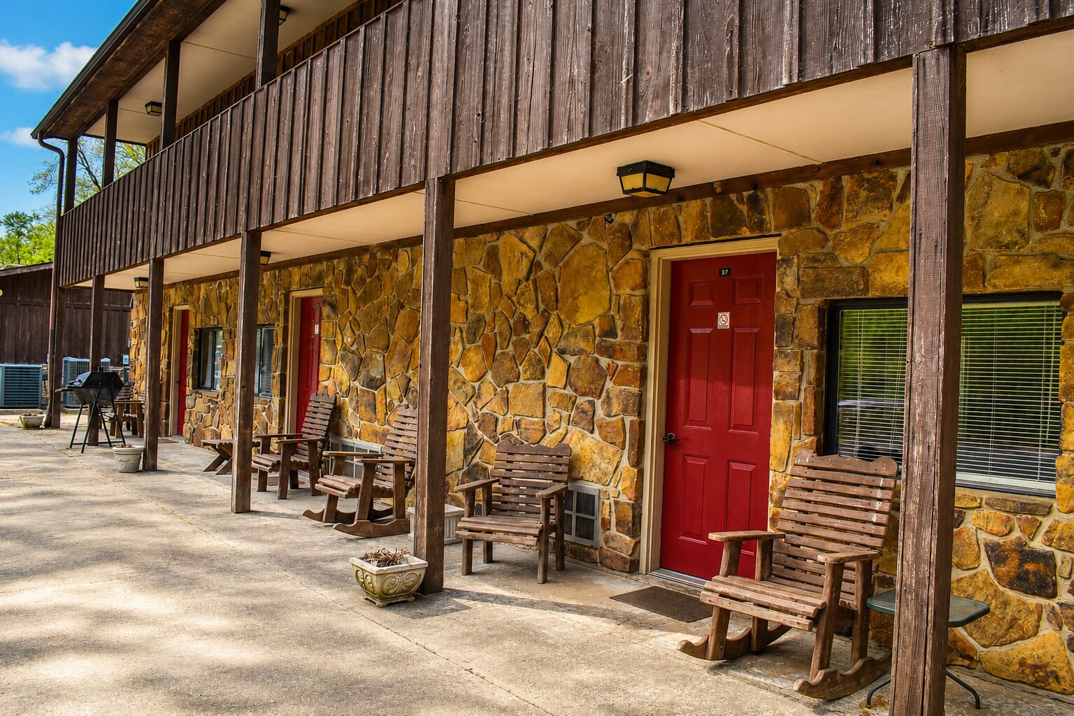 A stone building with a porch, red doors, and wooden furniture.