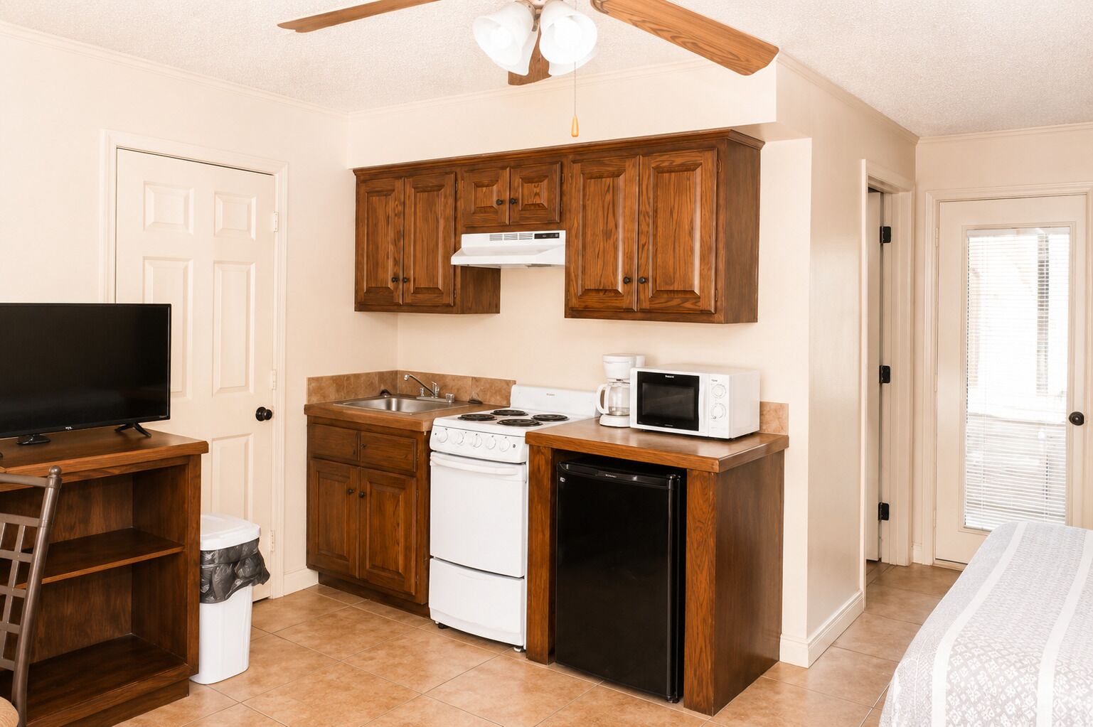A compact kitchen with wooden cabinets, a stove, microwave, and a small refrigerator.