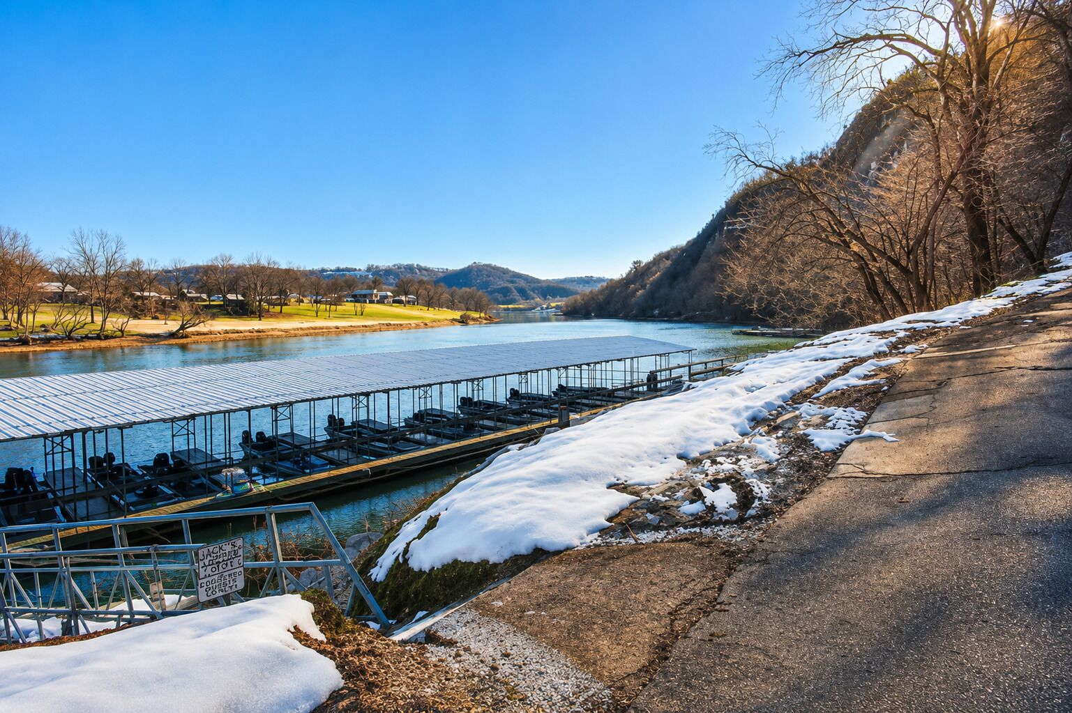 Un río con un muelle, nieve en el suelo y cielo despejado.