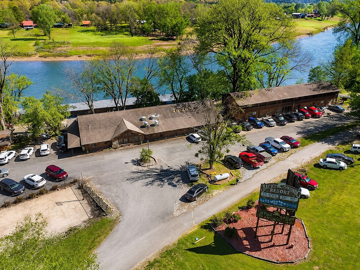 Vista aérea de un hotel con estacionamiento, un letrero que indica que es un complejo de golf, y una masa de agua al fondo.