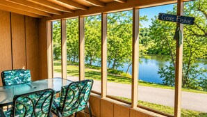 A dining area with a table and chairs, large windows with a view of a lake and trees, and a wooden ceiling. - Jack's White River Fishing Resort (Mountain View)