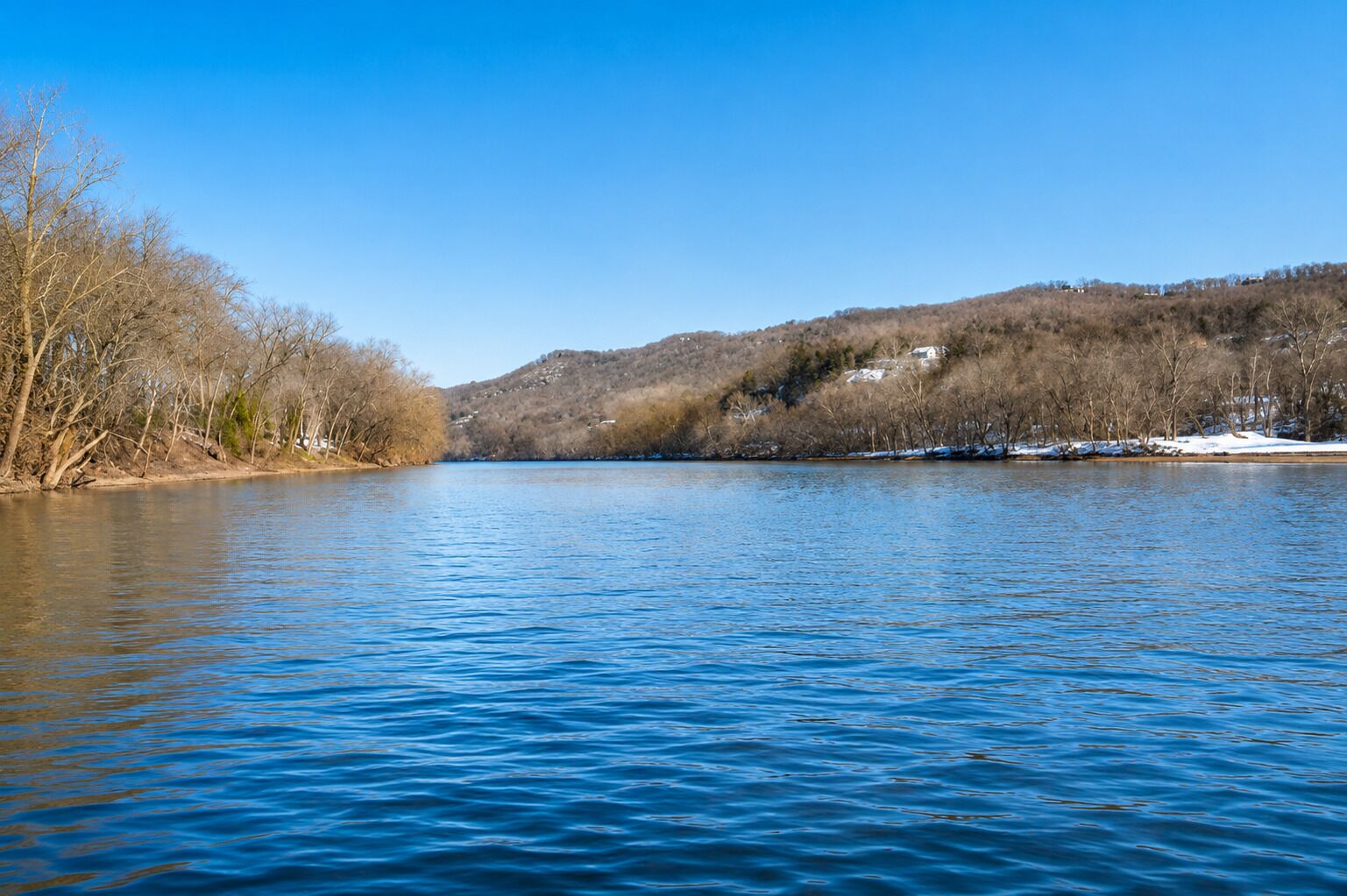 A calm river with trees on the banks and a hill in the background.