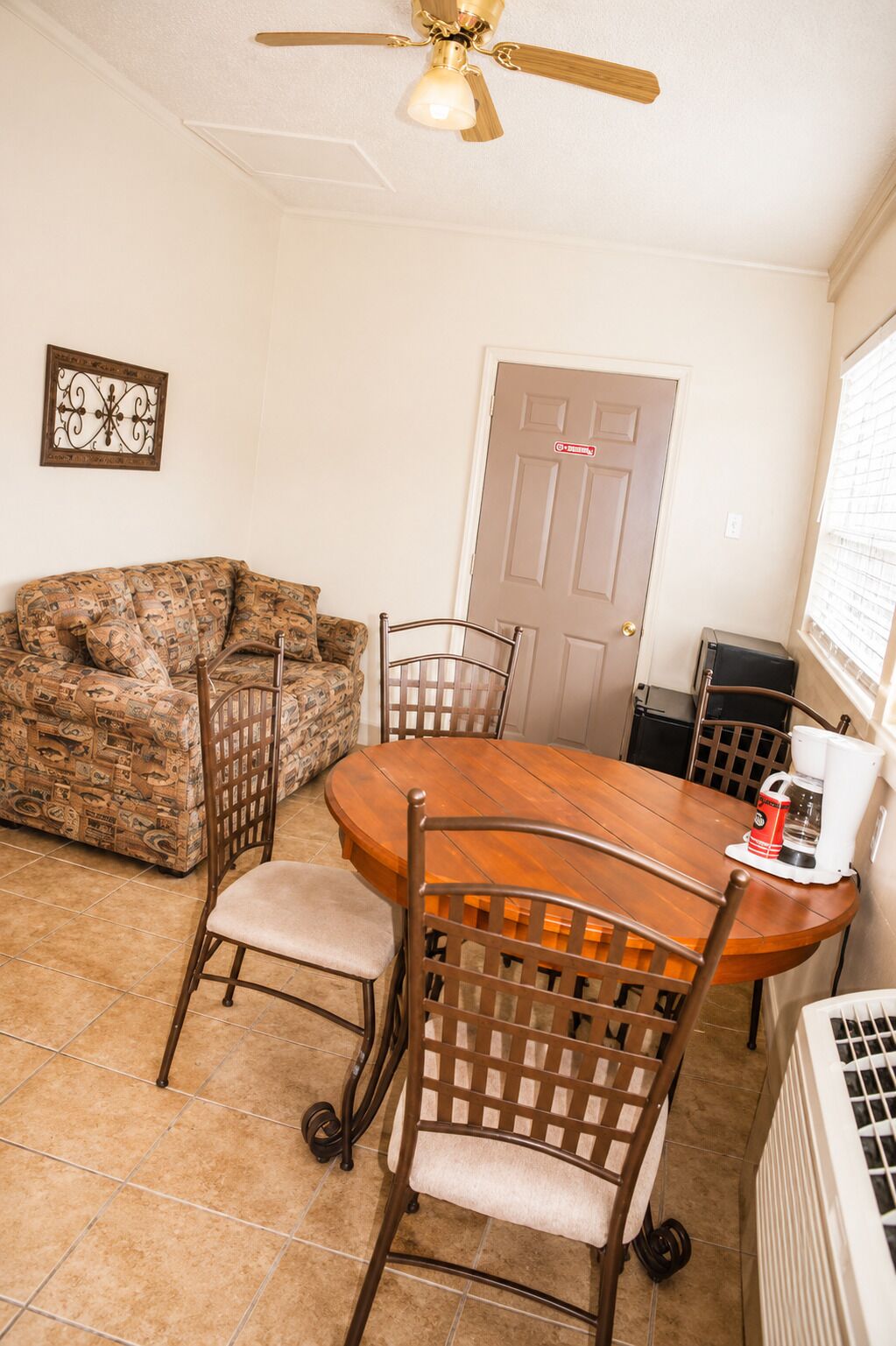 A dining area with a wooden table, four chairs, a ceiling fan, a door, and a radiator.
