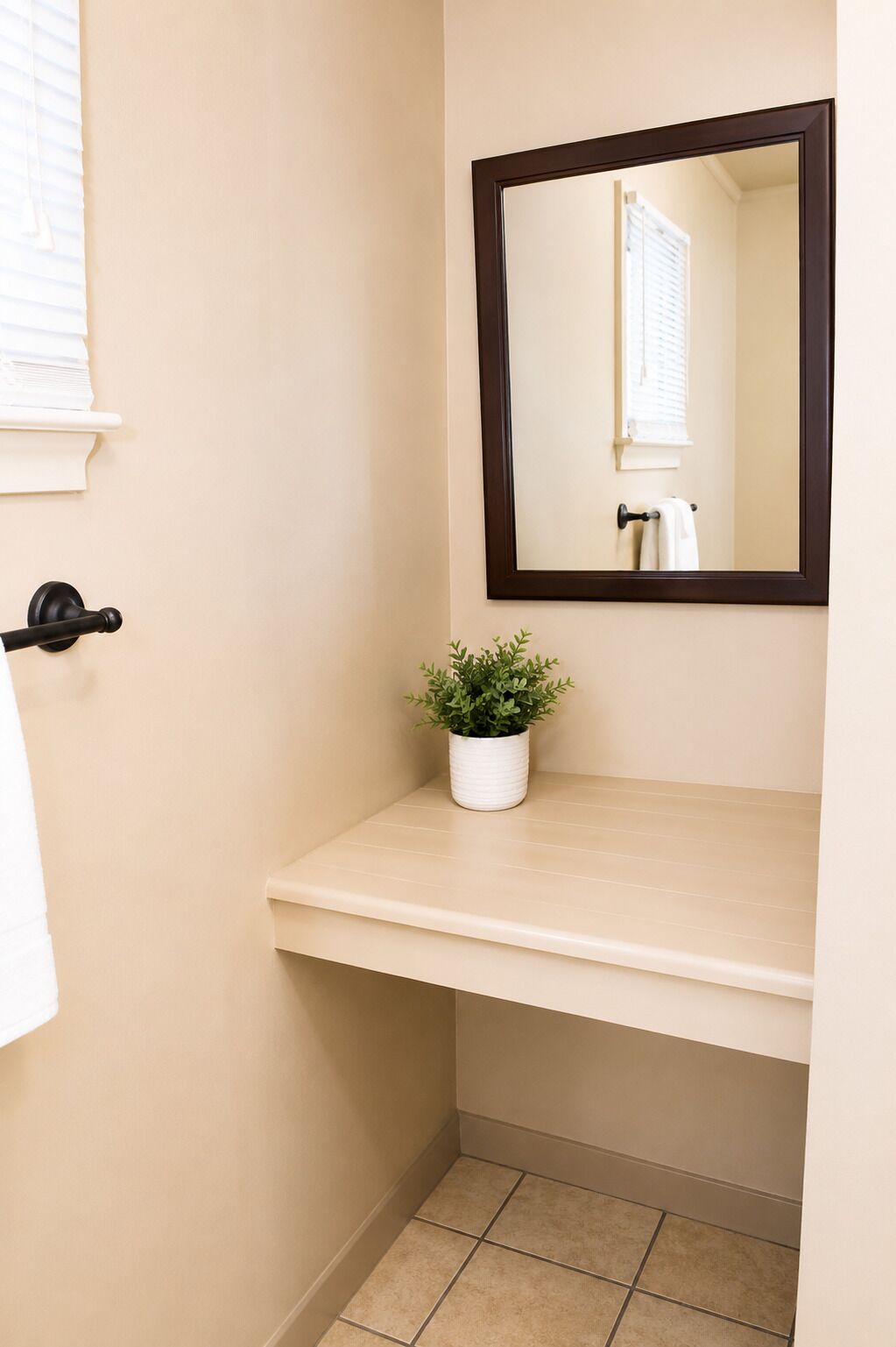 Une salle de bain avec un mur de couleur beige, un lavabo blanc, une plante en pot, un miroir et un porte-serviettes.